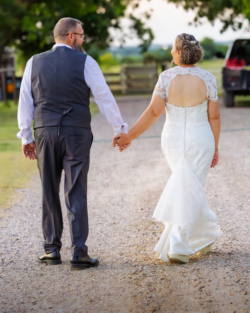 rustic-outdoor-wedding-texas-husband-wife-first-walk A husband and wife walking down a gravel road away from the camera after getting married.